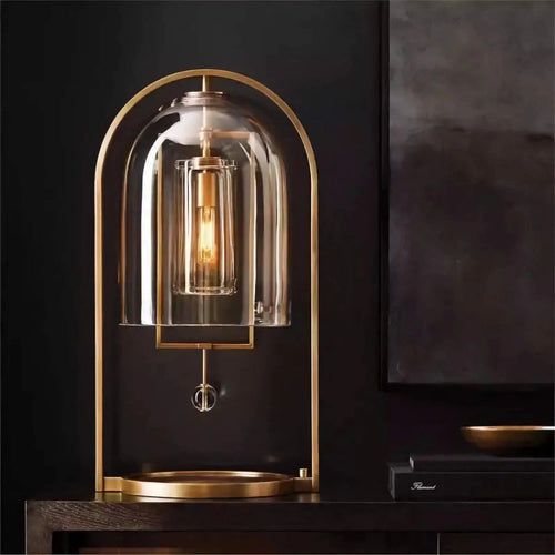 Aurelies Table Lamp featuring a clear glass lantern shade suspended within a brass frame, a luxury designer table lamp for contemporary and Mid-Century inspired interiors