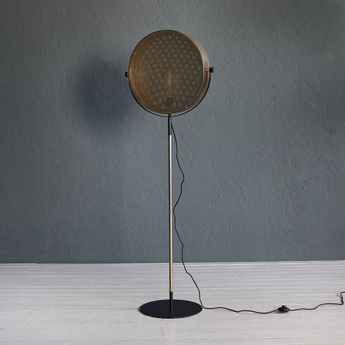 Gold industrial floor lamp with perforated spotlight shade and modern metal stand in a contemporary interior.