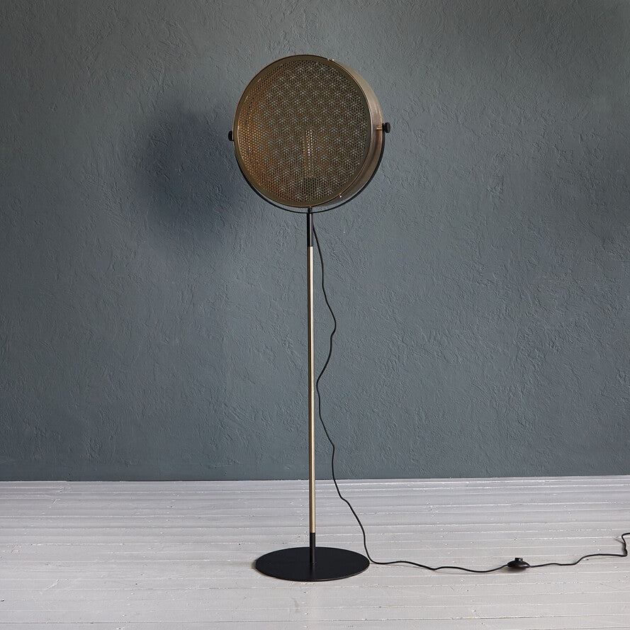 Gold industrial floor lamp with perforated spotlight shade and modern metal stand in a contemporary interior.