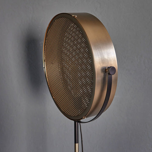 Gold industrial floor lamp with perforated spotlight shade and modern metal stand in a contemporary interior.